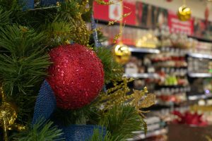 Red bauble on the Christmas tree against the background of defocus shelves in the store. Concept Christmas holiday sale New Year. Christmas decorations in the supermarket